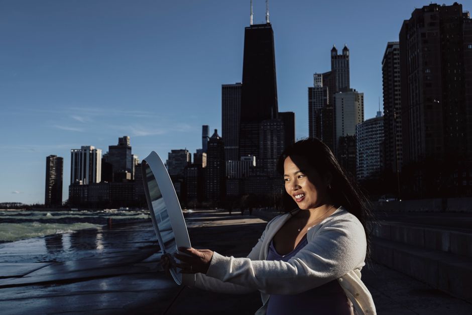 Asian woman smiling while holding a mirror against Chicago skyline, capturing a vibrant urban atmosphere.